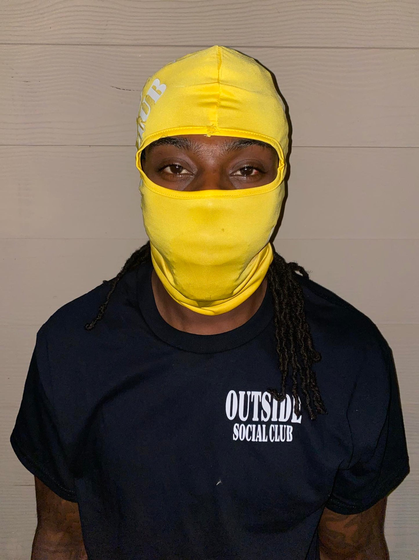 Person wearing a yellow balaclava and black 'Outside Social Club' t-shirt against a plain background