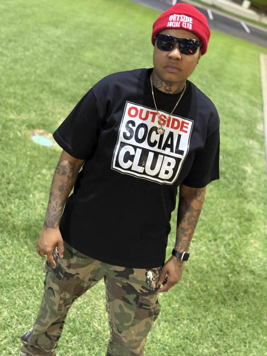 Human wearing a Black heavy weight graphic street T with “outside social club “ on the front 