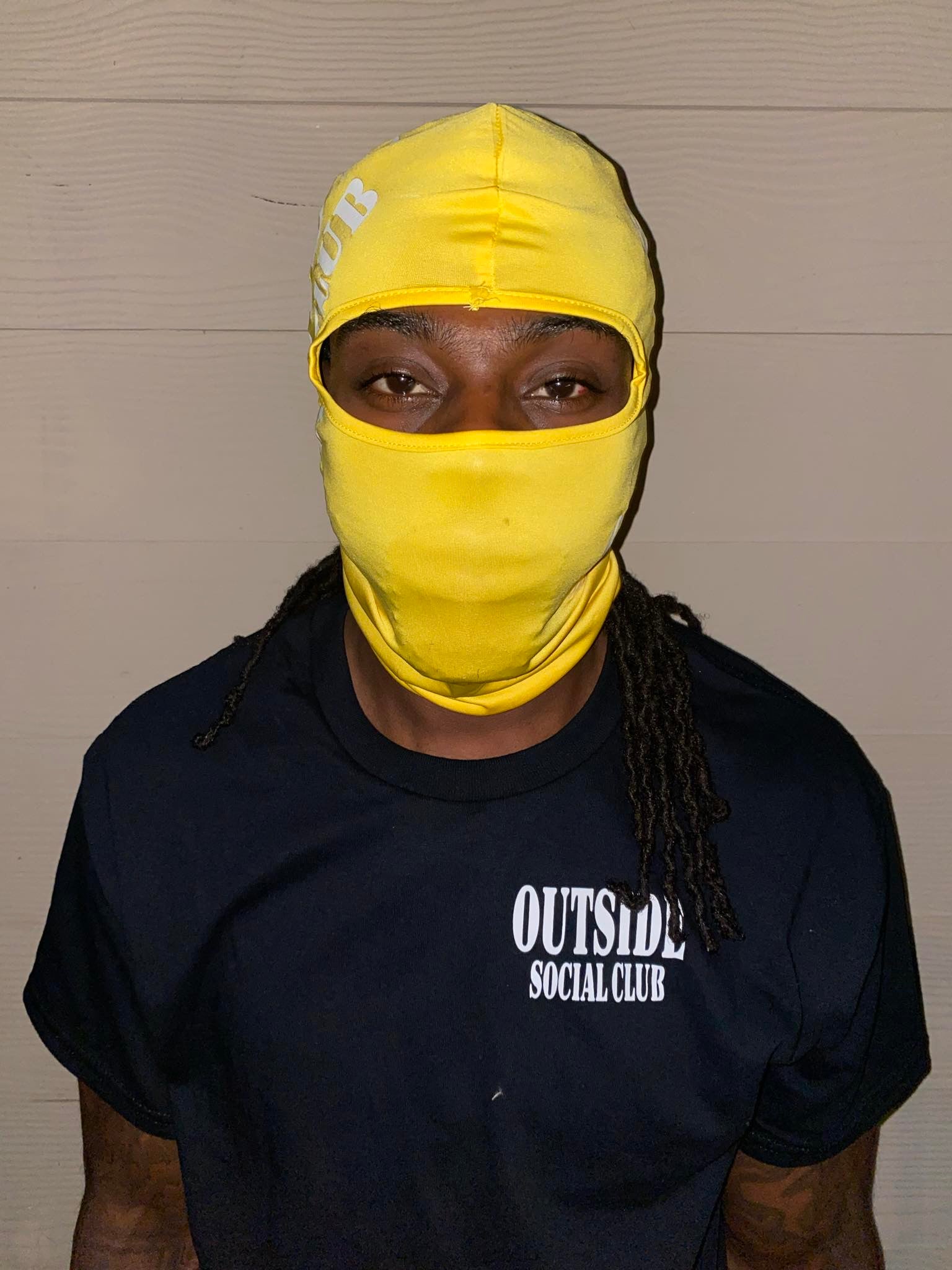 Person wearing a yellow balaclava and black 'Outside Social Club' t-shirt against a plain background